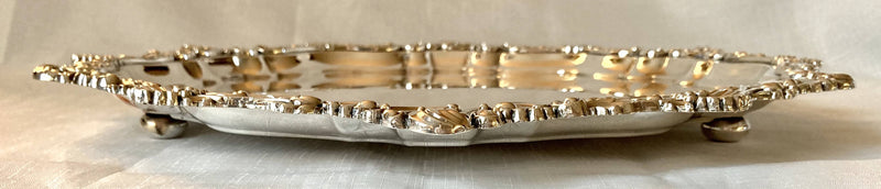 Large silver plated circular salver with shell and scroll border, raised on bun feet.